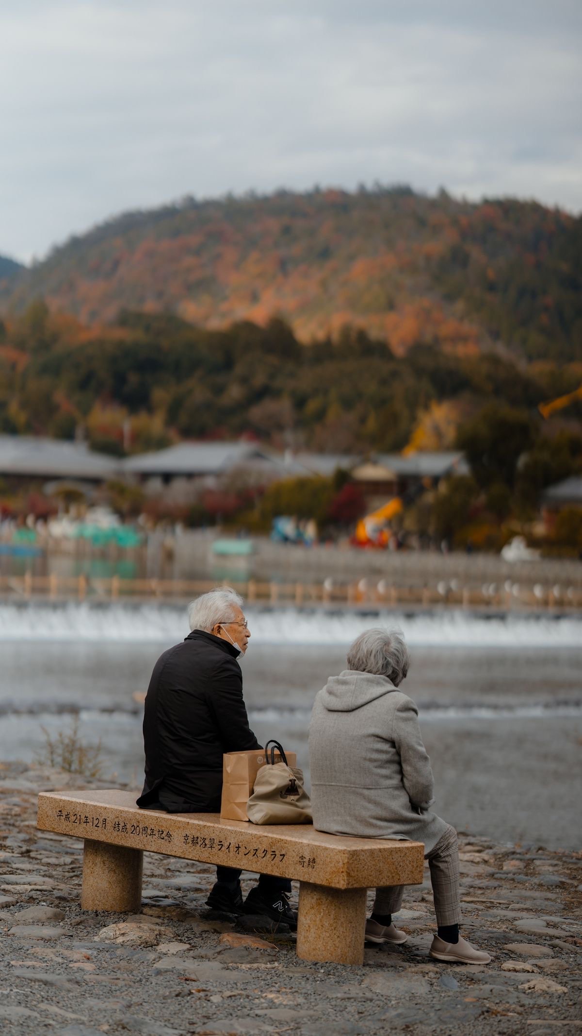 川辺のベンチに並んで座り、遠くを眺める日本の高齢のご夫婦